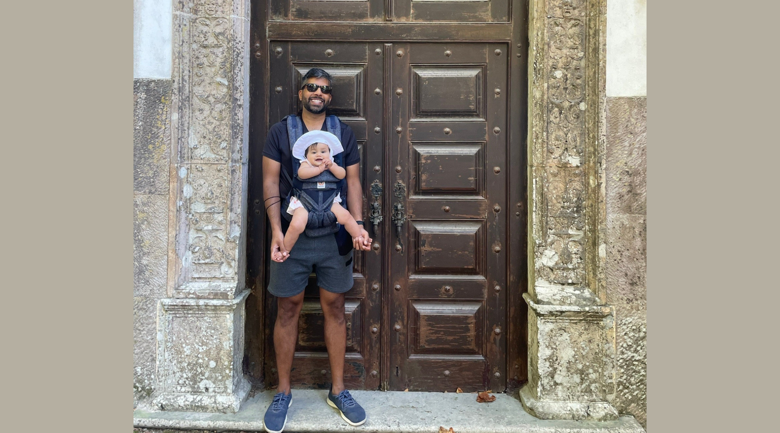 Dad wearing baby in front-carrier standing in front of ornate door.