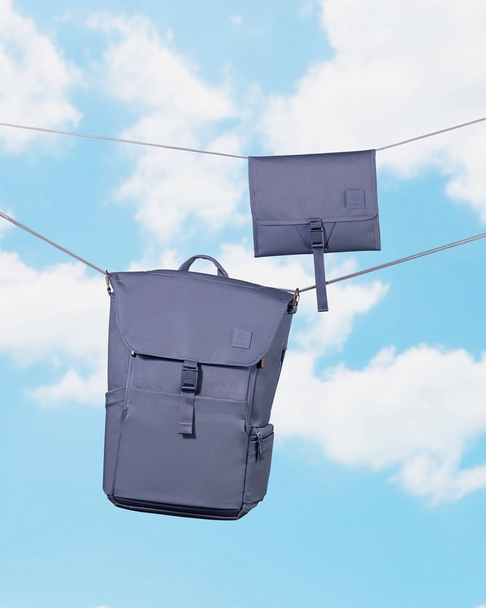 Blue diaper backpack and blue changing wallet attached to wires against a blue background with white clouds