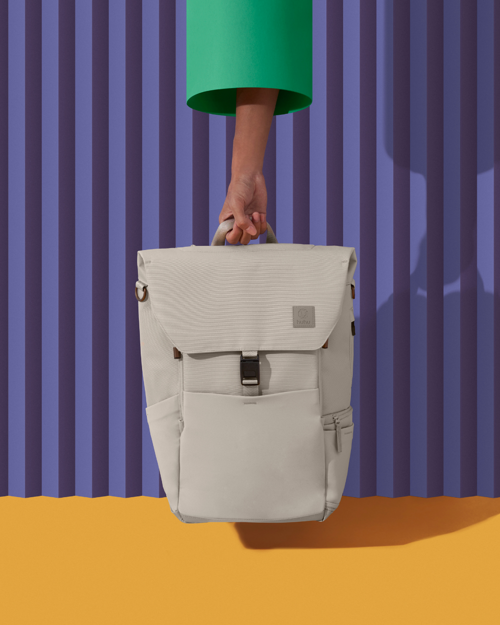 A hand holding a beige bag in front of a purple striped wall above orange ground.