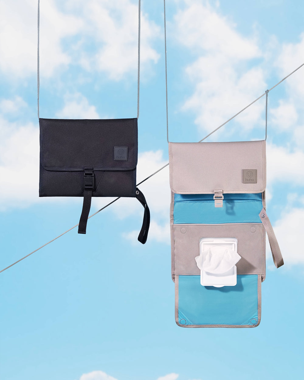 1 black and 1 taupe changing wallet hanging on wires against a blue background with clouds. The taupe wallet is open, showing wipes